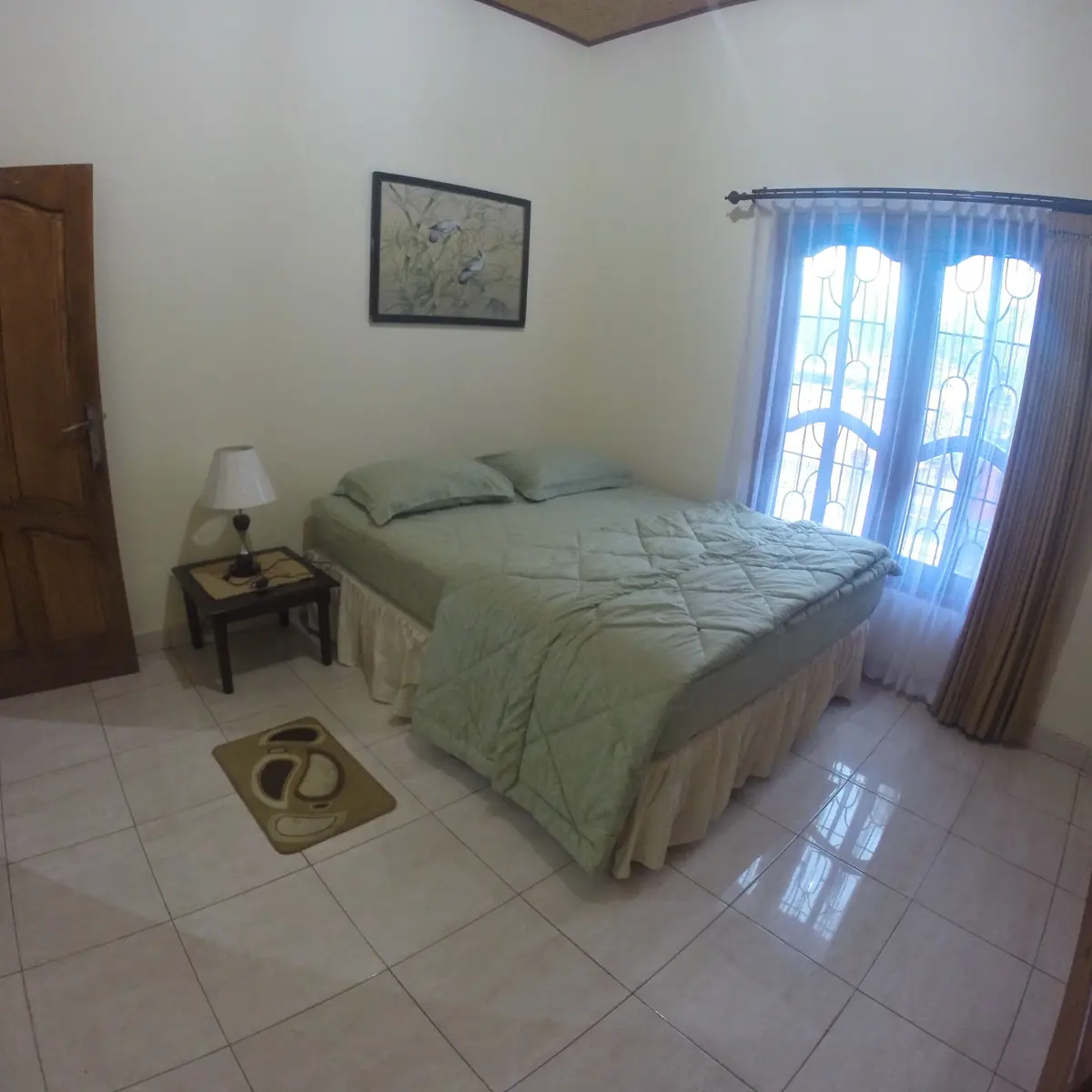 Bright guest bedroom with a bed, wooden door and curtained windows