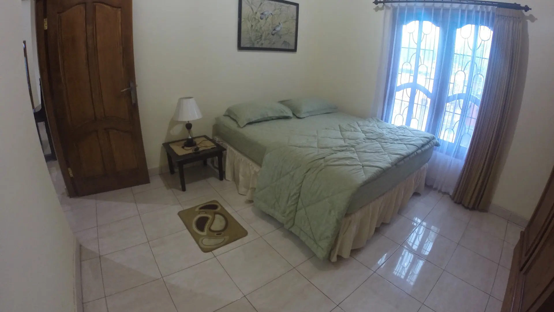 Bright guest bedroom with a bed, wooden door and curtained windows