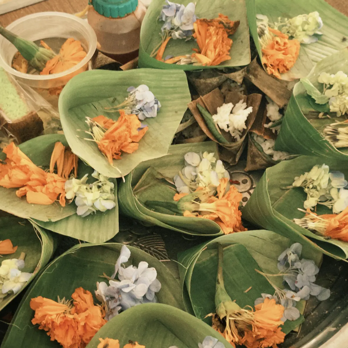 Rows of canang sari made from banana leaf with orange and white flowers