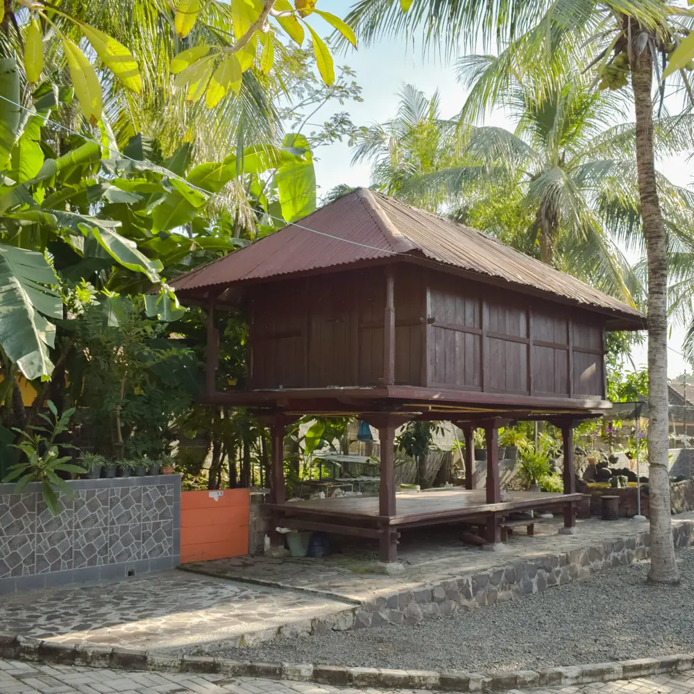A wooden lumbung, a raised rice barn, among banana plants and palms in the homestay garden