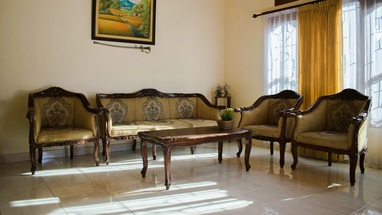 Lounge with carved wooden sofa and chairs beside tall windows