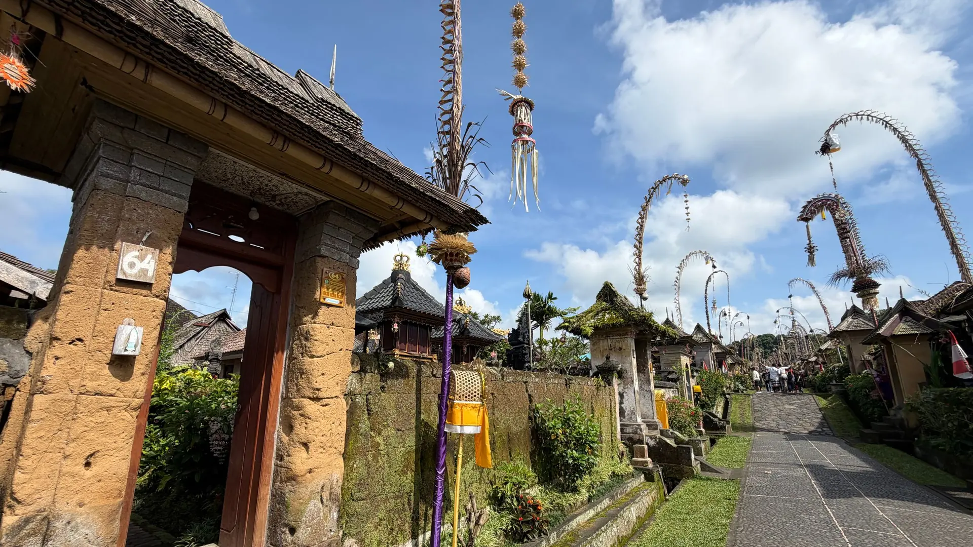 Village street with family gates and tall penjor bamboo poles