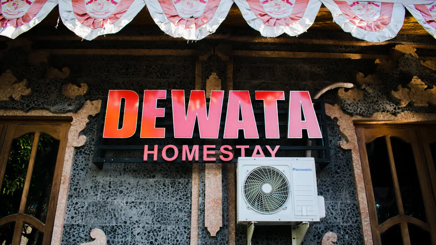 Red Dewata Homestay sign on a carved stone wall