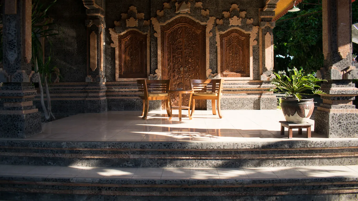 Shaded terrace with a table and chairs in front of carved doors